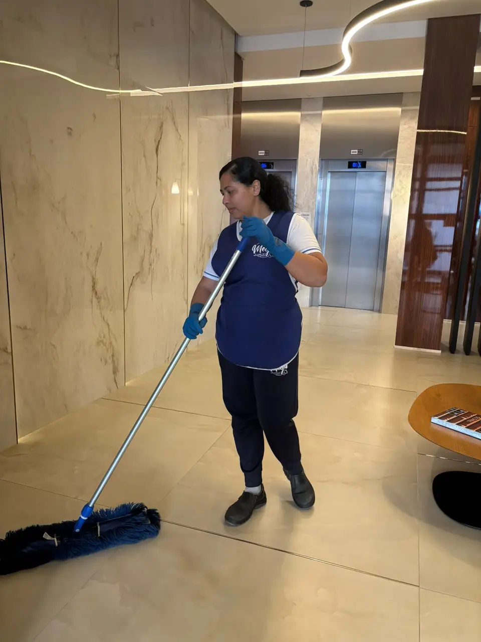 Colaboradora da Mega passando mop no piso do hall dos elevadores
